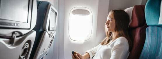 フランスへ向かう飛行機の中で座って携帯電話を見ている女性。