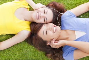 フランスの芝生に寝そべって音楽を聴く 2 人の女性。