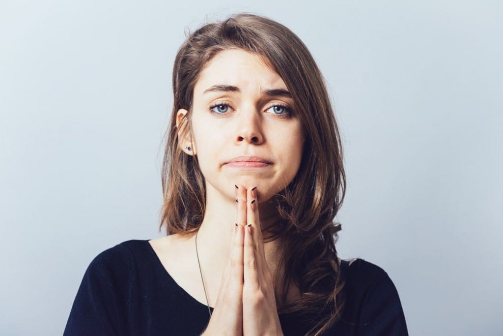 フランスで顔の前に手を当てて祈る若い女性。