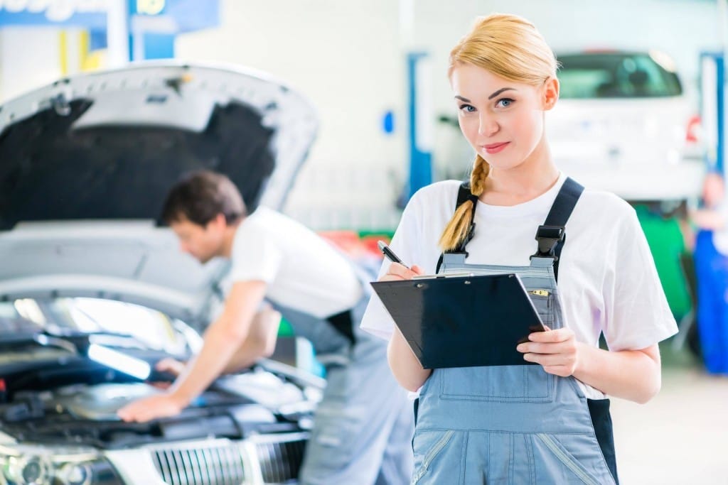 フランスで、オーバーオールを着た女性が車の前でクリップボードを持っています。