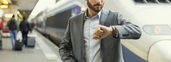 フランスの電車の横に立つ時計を持った男性。