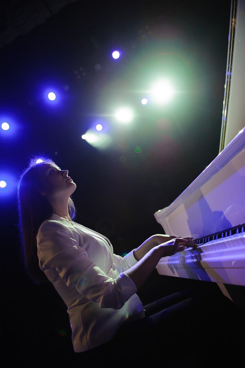 フランスの暗い部屋で白いピアノを弾く女性。
