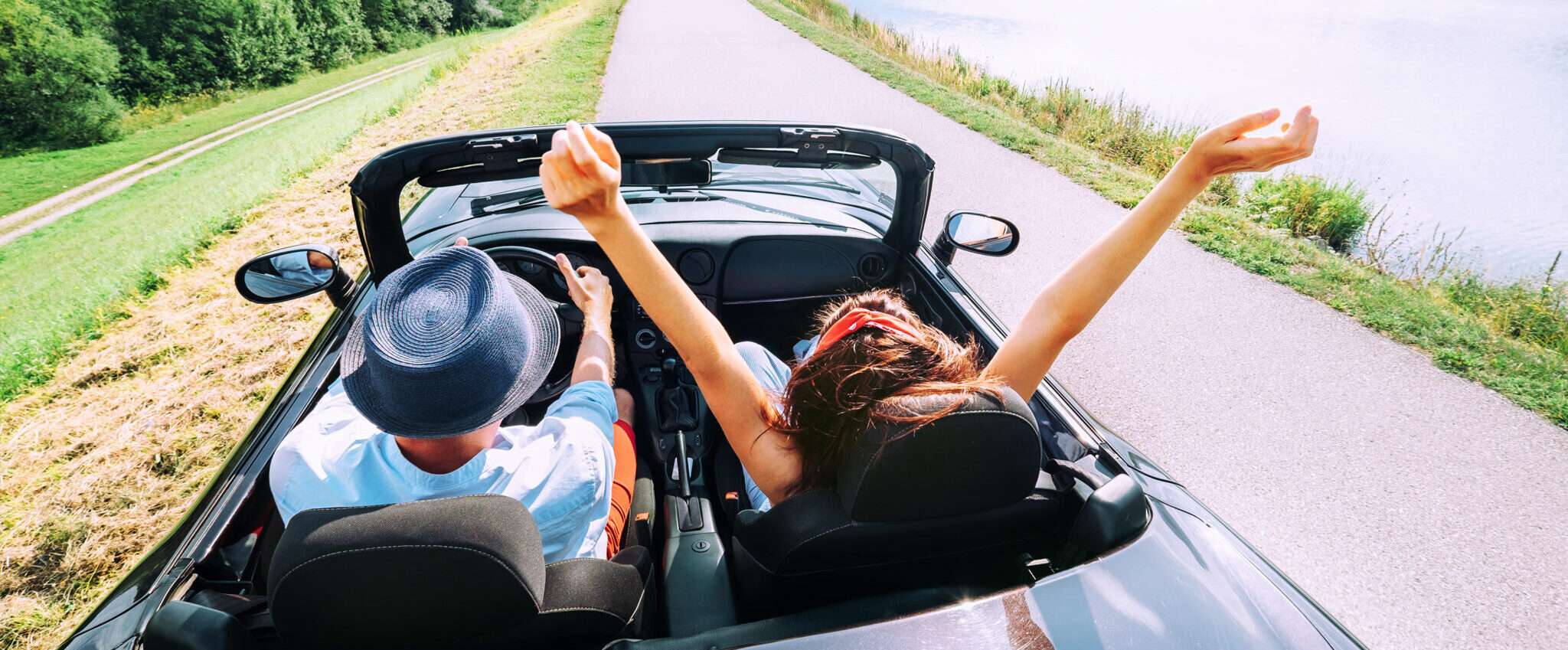 フランスの風光明媚な風景の中をオープンカーに乗り、純粋な喜びで腕を上げているカップル。