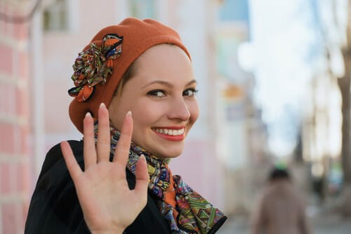 フランスで帽子とスカーフをかぶった女性が手を振っている。