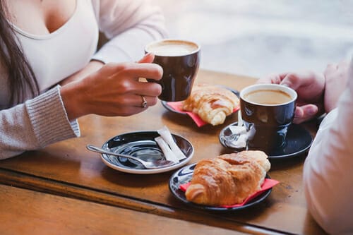 フランスで 2 人がコーヒーとクロワッサンを飲みながらテーブルに座っています。