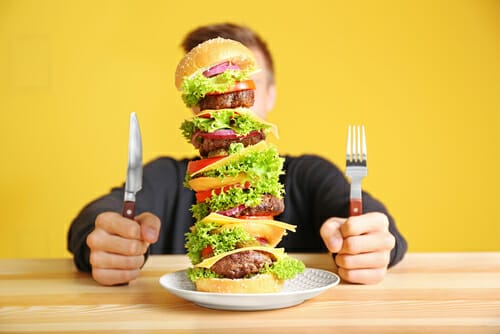 男性がフォークとナイフを使ってハンバーガーを食べています。