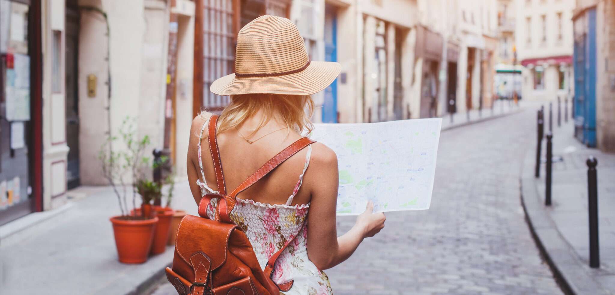 帽子をかぶった女性が地図を持ってフランスの通りを歩いています。