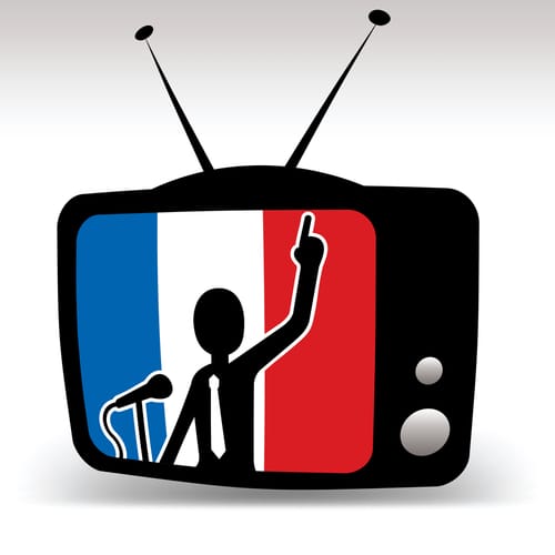 フランス国旗が掲げられたテレビとマイクを持った男性。