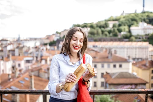 フランスの街を見下ろすバルコニーでバゲットを持つ女性。