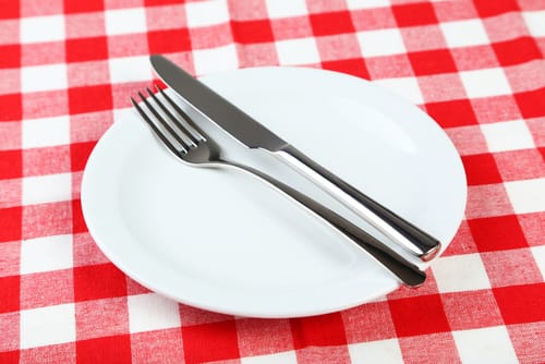 フランスを思わせる赤と白のチェック柄のテーブルクロスに、フォークとナイフがセットされた白いお皿。 フランスを思わせる赤と白のチェック柄のテーブルクロスに、フォークとナイフがセットされた白いお皿。