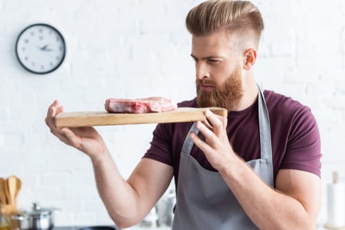 フランスで、ひげを生やした男性がまな板の上で肉片を持っています。