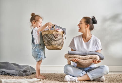 フランスの伝統的な衣装を着た女性とその娘が、衣類の入ったバスケットを持って床に座っている。