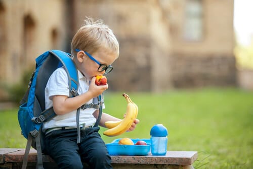 フランスでベンチに座ってバナナと果物を食べる少年。