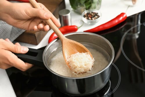 フランスのエプロンを着た人がコンロの上の鍋でご飯をかき混ぜています。