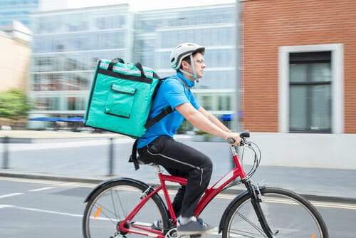 配達用のバッグを背負って自転車に乗るフランス人の男性。