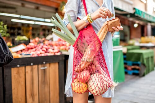 フランスから来た女性が野菜の入った赤い袋を持っています。