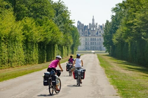 フランスの城の前の道を自転車に乗って走る人々のグループ。