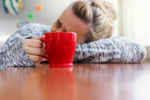 フランスで、女性が赤いコーヒーマグを持ってテーブルに横たわっている。