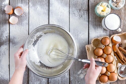 フランスで、女性が木製のテーブルの上のボウルで卵と小麦粉を混ぜている。