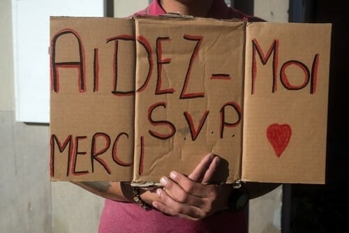 フランスのaides-moi merci SVPと書かれた看板を掲げる男性。