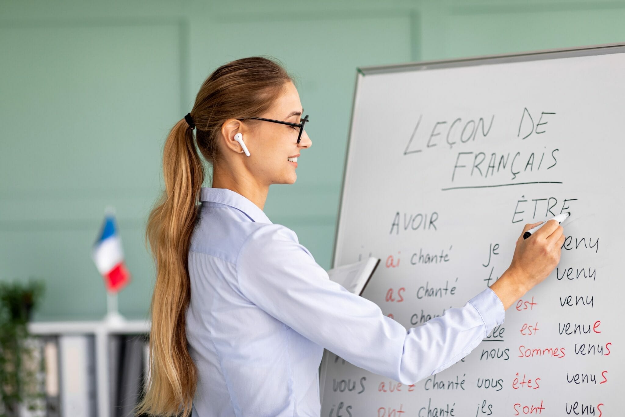 フランス語の教室で女性がホワイトボードに字を書いている。