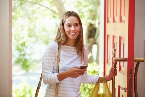 フランスのドアの前で買い物袋と携帯電話を持つ女性。