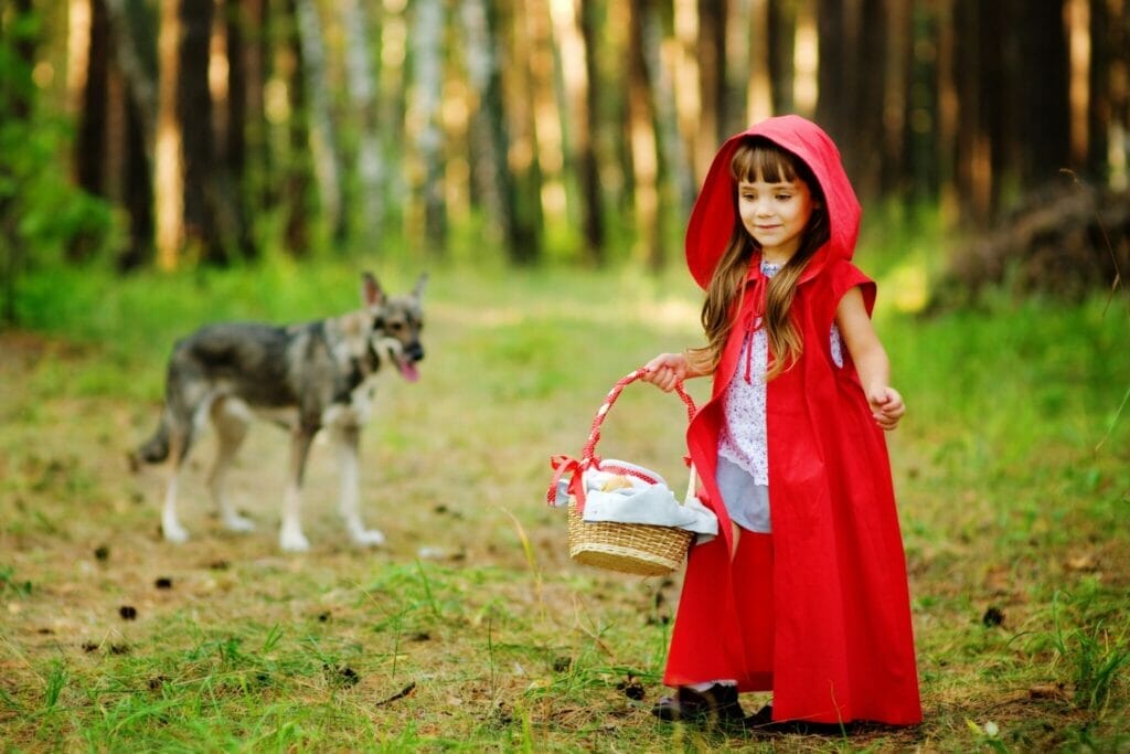 フランスで、赤ずきんちゃんの衣装を着た少女が犬と一緒に森の中に立っています。