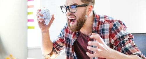 しわくちゃの紙の山の前でコンピューターに向かうフランス人男性。