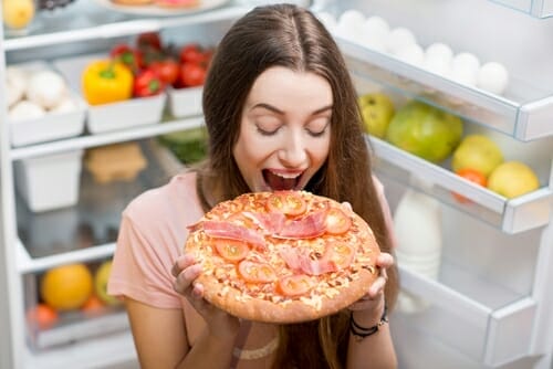 フランスから来た女性が、開いた冷蔵庫の前でピザを持っています。