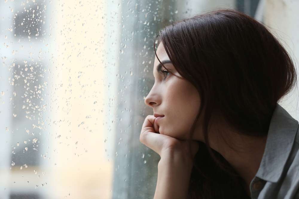 顔に雨粒がついたフランスで窓の外を眺める女性。