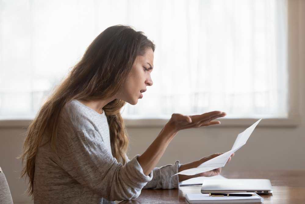 フランスのテーブルに座っている女性が書類を読みながらイライラしている様子だ。