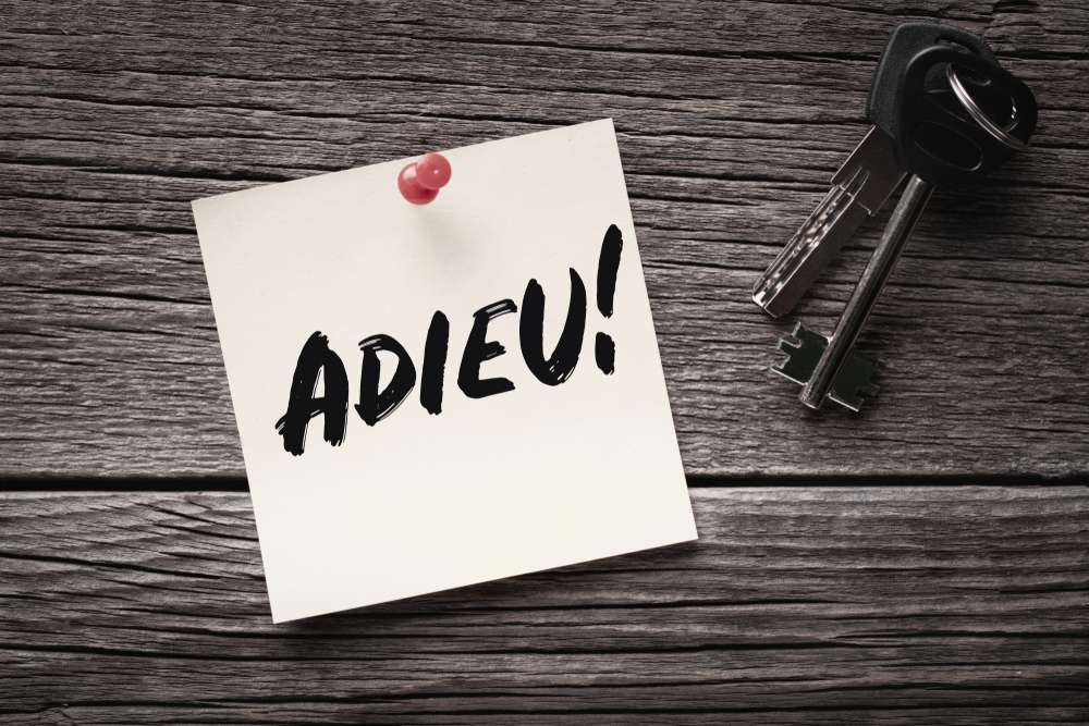 「ADIEU!」と書かれた手書きのメモが木の表面にピンで留められており、フランス風の雰囲気が漂っています。この心のこもった別れの右側には鍵が 2 つ置かれています。.