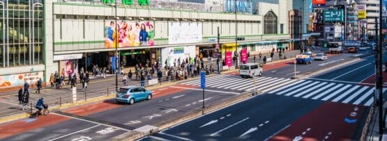 晴れた日の東京の新宿駅の都市のストリートビュー。歩行者、車両、周囲の建物が見える。近くのフランス語教室マンツーマンでは、新宿の賑やかなエネルギーの中で、個人に合わせたフランス語レッスンを提供しています。.