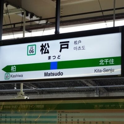 駅の標識には柏と北千住の方向が表示され、中央に松戸駅が強調されています。数字と日本語の文字がシーンを囲み、フランス語教室マンツーマンの設定を思い出させます。そこでは、すべてが明確に定義されながらも相互に接続されています。.