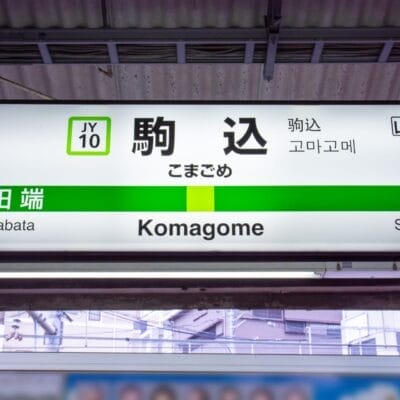 駒込駅の標識には、田端（JY09）と巣鴨への道順が日本語、英語、韓国語で表示されています。賑やかな通りへ向かう場合でも、近くのフランス語のプライベートレッスンへ向かう場合でも、多言語の案内で簡単に移動できます。.