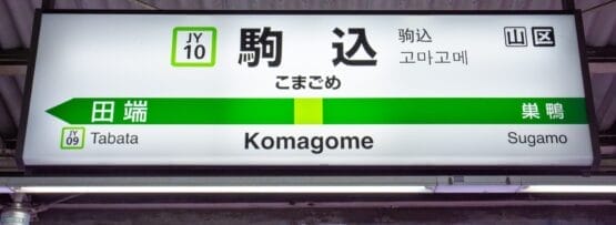 駒込駅の標識には、田端（JY09）と巣鴨への道順が日本語、英語、韓国語で表示されています。賑やかな通りへ向かう場合でも、近くのフランス語のプライベートレッスンへ向かう場合でも、多言語の案内で簡単に移動できます。.