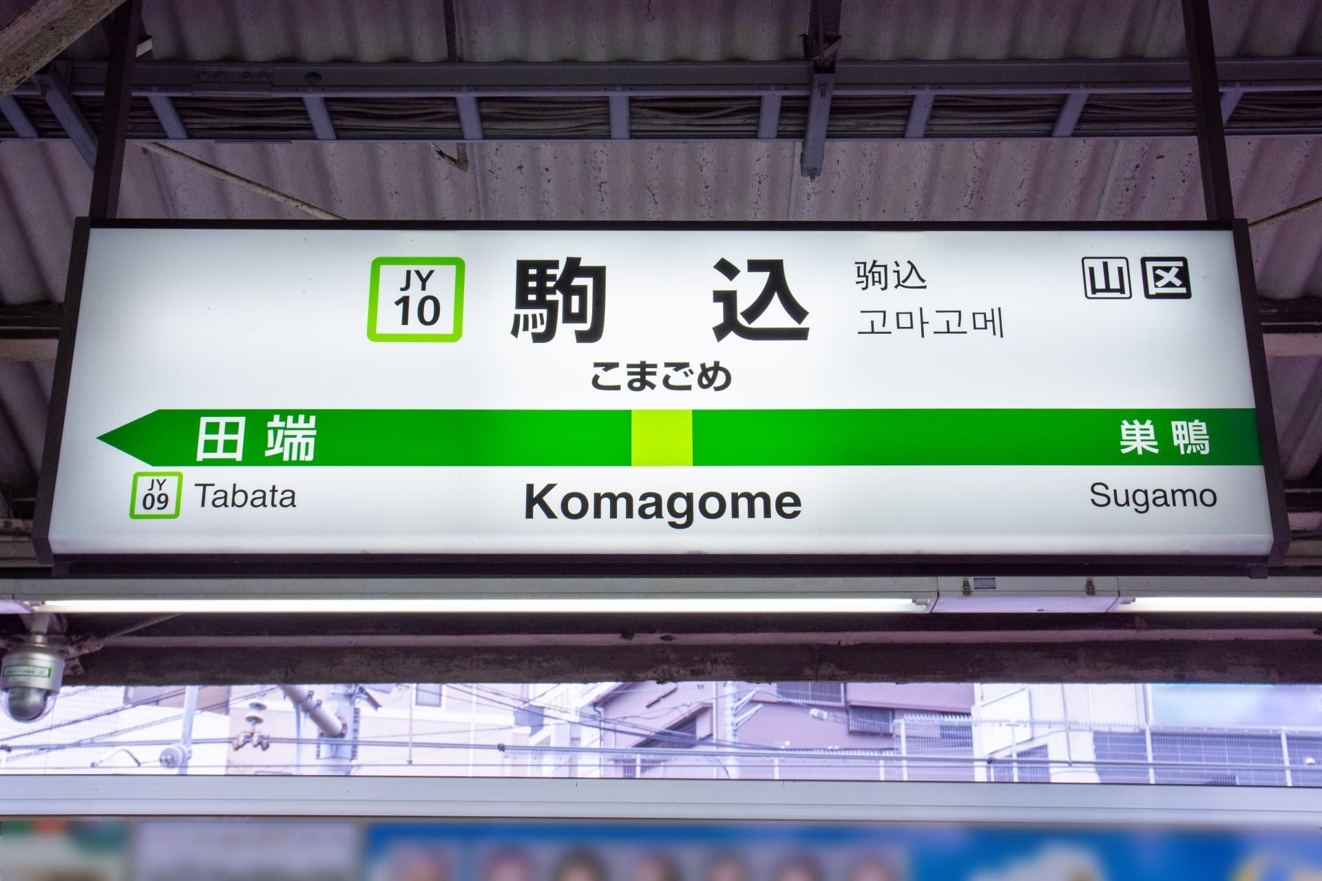 駒込駅の標識には、田端（JY09）と巣鴨への道順が日本語、英語、韓国語で表示されています。賑やかな通りへ向かう場合でも、近くのフランス語のプライベートレッスンへ向かう場合でも、多言語の案内で簡単に移動できます。.
