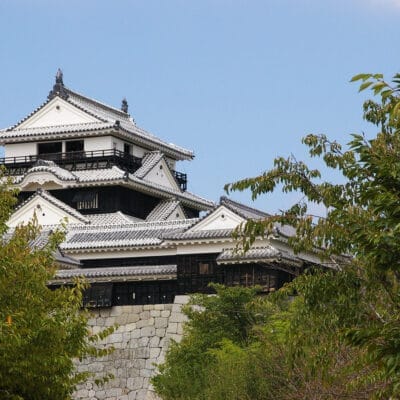 伝統建築の日本の城が堂々と建っており、三重の屋根と石の基礎が特徴で、フランス語教室マンツーマン愛媛・松山で培われた洗練された気品によく似ています。澄んだ青い空の下、緑豊かな木々に囲まれ、さまざまな文化が融合した穏やかな場所です。.