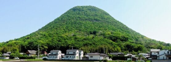 高松の澄み切った青空の下、住宅や畑の集落の背後に緑の円錐形の丘がそびえ立ち、香川の絵のような魅力を彷彿とさせます。.