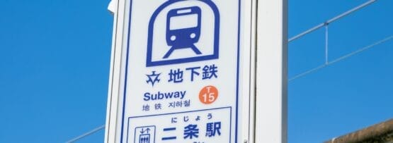 地下鉄のアイコンと日本語、英語、フランス語教室マンツーマンの文字が描かれた二条駅の標識が、澄んだ青空に堂々と立っています。.