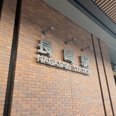 レンガの壁には日本語と英語で「長崎駅」の標識が飾られ、スラット屋根の下に収まっています。.