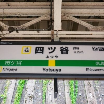 東京の四ツ谷の駅標識。市ヶ谷駅と信濃町駅の日本語の文字と英語のラベルが特徴です。通勤に文化的な雰囲気を加える、フランス語教室マンツーマンなどの近くのサービスに注目するのに最適なスポットです。.