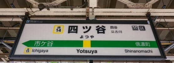 東京の四ツ谷の駅標識。市ヶ谷駅と信濃町駅の日本語の文字と英語のラベルが特徴です。通勤に文化的な雰囲気を加える、フランス語教室マンツーマンなどの近くのサービスに注目するのに最適なスポットです。.