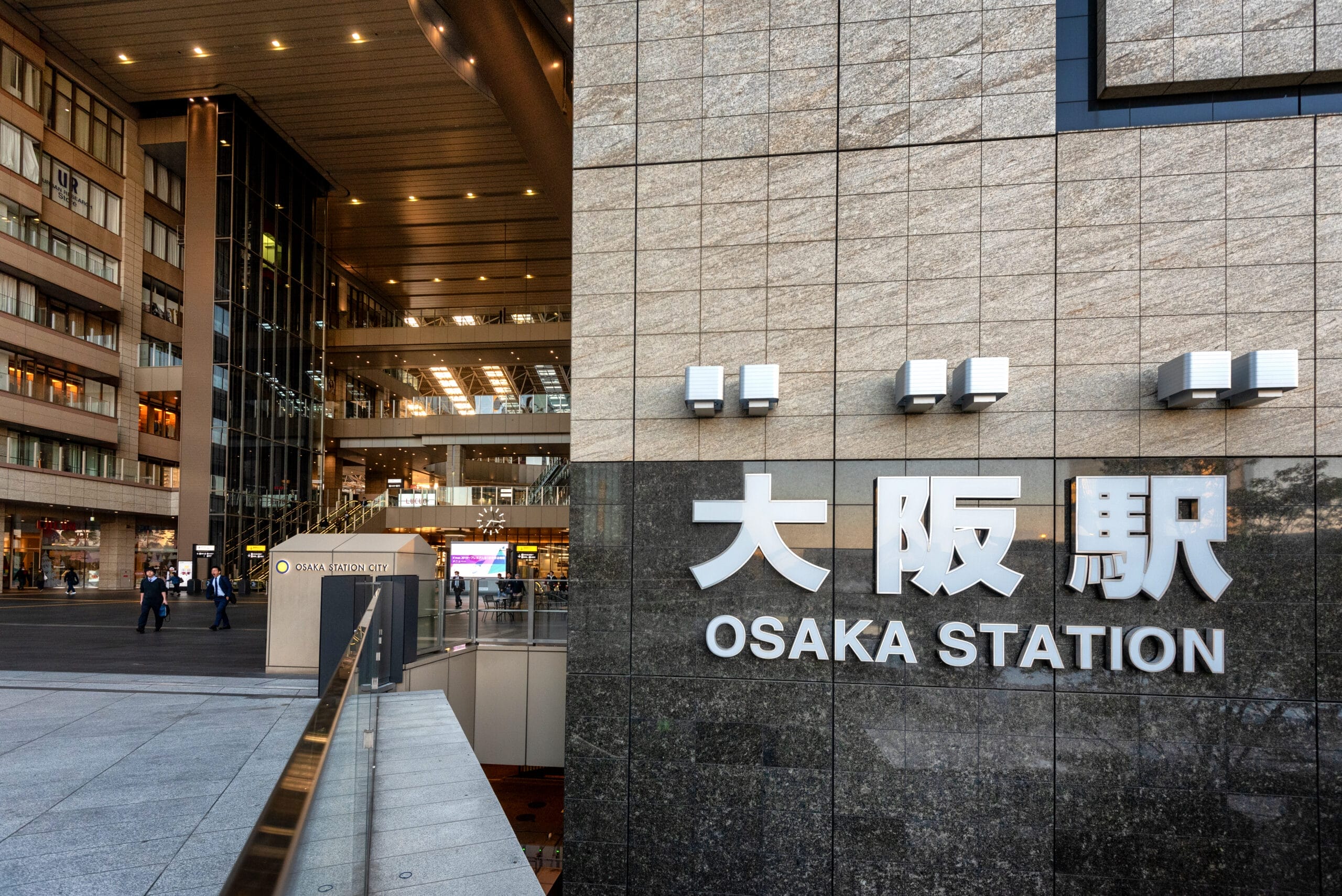 大阪駅の外観は、モダンな建築と日本語と英語の大きな看板がひときわ目を引きます。近くでは、おそらくこの活気ある中心地の便利な場所にあるフランス語教室マンツーマンに向かう人々が賑わっています。.