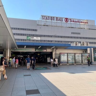 行き交う人で賑わう柏のステーションモールの入り口。高島屋の看板が頂上に飾られたこの建物は、晴れた空の下、タイル張りの前景を見せて立っています。近くのフランス語教室マンツーマンでは、個人に合わせた語学レッスンを提供しています。.