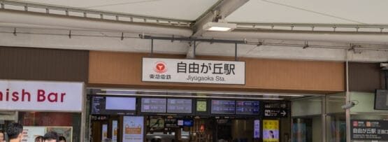 大きな白い天蓋の下、自由が丘駅の入り口に向かって歩く人々。入口の上には駅名標が見えており、次の目的地に向かう人や、近くにフランス語教室マンツーマンがある人を歓迎する雰囲気を醸し出しています。.