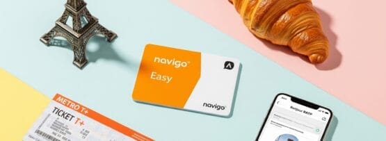 カラフルなパステルカラーの背景に、Navigo Easyトランジットカード、メトロの切符、ミニチュアのエッフェル塔、クロワッサン、交通アプリの入ったスマートフォンが配置されている。.