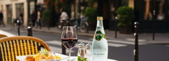 ステーキ、フライドポテト、赤ワイン、ペリエが置かれたレストランのテーブル。.